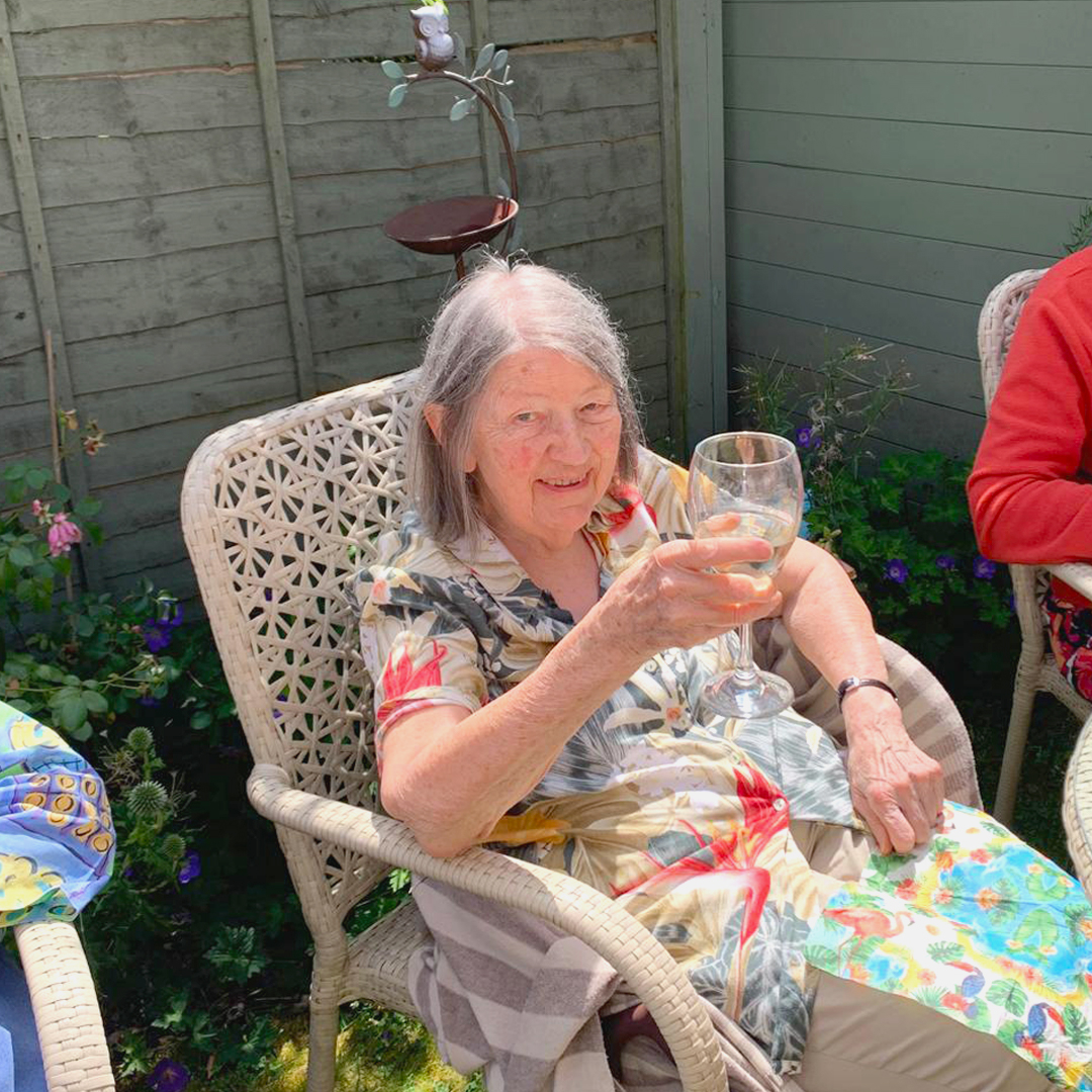 A happy resident smiles and raises a glass of wine while sat in the sun at the summer party